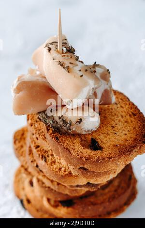 La nourriture. Une tour de pain grillé croustillant aux olives et des canapés au jambon et au fromage à la crème sur un élégant blanc et un fond textural. Pain grillé croustillant pour le timbre Banque D'Images