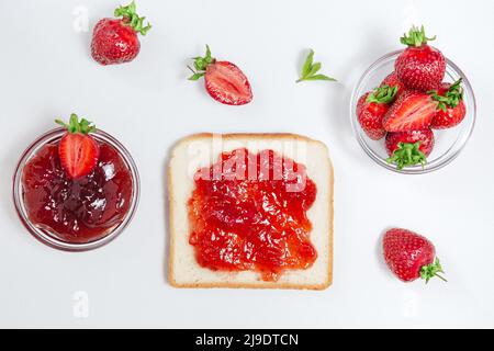 Toasts avec confiture de fraises pour le petit déjeuner sur fond blanc. Vue de dessus. Mûrir les fraises fraîches et la confiture de fraises maison, étaler sur le pain. Banque D'Images