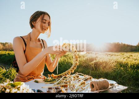 Portrait de la belle femme faisant couronne de fleurs pissenlits sur le champ de floraison. Style de vie d'été, amoureux de la nature et concept de liberté. Fleuriste Banque D'Images