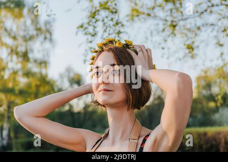 Portrait d'une belle femme confiante avec couronne de fleurs pissenlits sur la tête. Style de vie d'été, amoureux de la nature et concept de liberté. Atelier de fleuriste. Banque D'Images