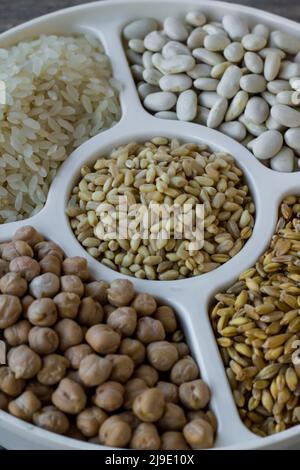 Pois chiches séchés non cuits, blé, riz et haricots blancs dans une assiette divisée sur une surface en bois Banque D'Images