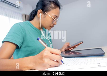 La jeune femme écrit sur papier des exemples mathématiques et regarde dans les appareils électroniques Banque D'Images