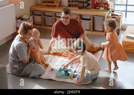 Grande famille dans une salle de jeux ensoleillée. Parents jouant avec des enfants et des jouets. Joyeux temps avec les jeux. Mère père fils filles dans une maison moderne colorée Banque D'Images