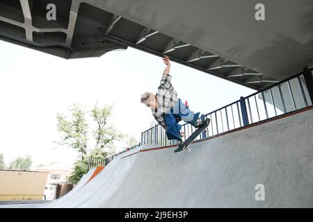Portrait d'un garçon adolescent à bord d'un skateboard et faisant des tours sautant dans l'air au skate Park en plein air Banque D'Images