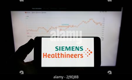 Personne tenant un téléphone portable avec le logo de la société allemande Siemens Healthineers AG à l'écran en face de la page Web d'affaires. Mise au point sur l'affichage du téléphone. Banque D'Images