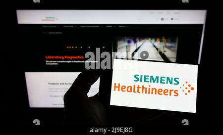 Personne tenant le téléphone portable avec le logo de la société allemande Siemens Healthineers AG sur l'écran en face de la page web d'affaires. Mise au point sur l'affichage du téléphone. Banque D'Images