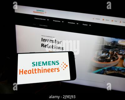 Personne tenant un smartphone avec le logo de la société allemande Siemens Healthineers AG à l'écran devant le site. Mise au point sur l'affichage du téléphone. Banque D'Images