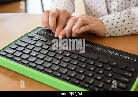 Une femme aveugle utilise un ordinateur avec un écran en braille et un clavier d'ordinateur. Périphérique inclus. Banque D'Images