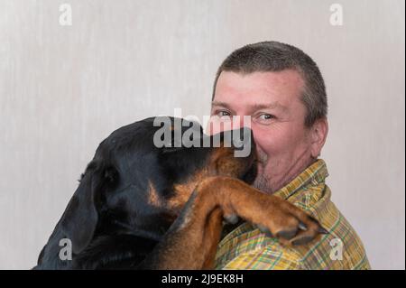 Portrait d'un heureux adulte qui câlin son grand chien noir. Homme avec une coupe courte et des cheveux grisants. Une femme Rottweiler met son patte sur son épaule Banque D'Images