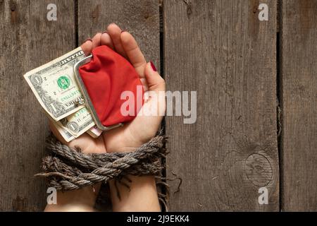 Portefeuille rouge avec dollars américains dans les mains liées de la fille sur la table Banque D'Images