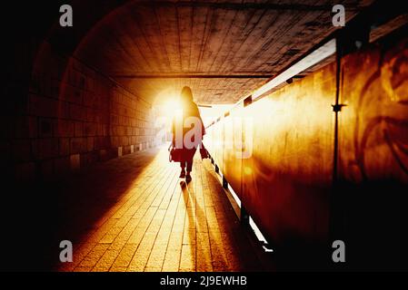 Vue arrière de la silhouette d'une femme dans un tunnel avec des rayons du soleil au coucher du soleil, une femme marchant seule dans la rue de la ville Banque D'Images