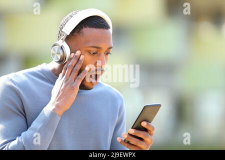 Un homme choqué avec un casque sans fil et un smartphone dans la rue Banque D'Images