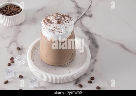 café froid avec lait au chocolat et glace, crème fouettée et cannelle dans un verre sur une table en marbre. dessert d'été froid Banque D'Images