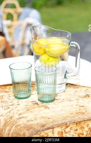 Verseuse d'eau pleine d'eau et de citrons avec deux verres dans le cadre du jardin extérieur Banque D'Images