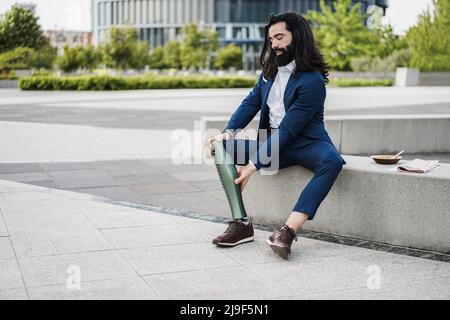 Homme d'affaires qui ajuste sa jambe prothétique à l'extérieur du bâtiment de bureau - se concentrer sur les mains tenant la prothèse Banque D'Images