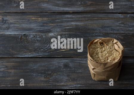 Riz brun brut à grain long dans un sac de papier sur fond en bois, espace Banque D'Images