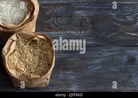 Riz basmati blanc et brun à grain long cru dans un sac de papier sur un fond en bois, espace Banque D'Images