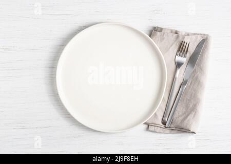 Assiette blanche vide et couverts argentés sur la serviette de table en bois blanc. Banque D'Images