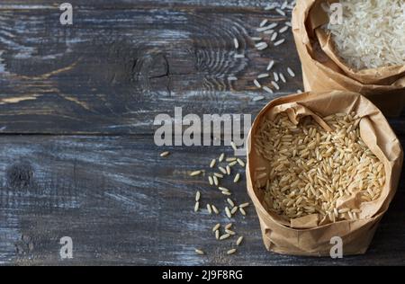 Riz basmati blanc et brun à grain long cru dans un sac de papier sur un fond en bois, espace Banque D'Images