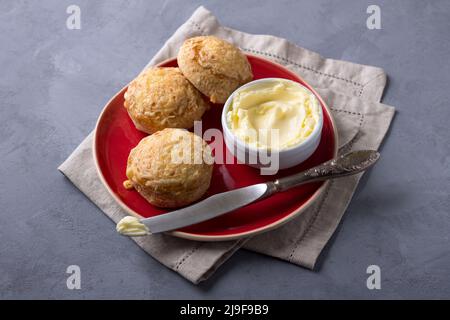 Scones maison fraîchement cuits avec du fromage et des herbes sur une assiette rouge avec du beurre sur un fond texturé gris. Petits pains traditionnels anglais Banque D'Images