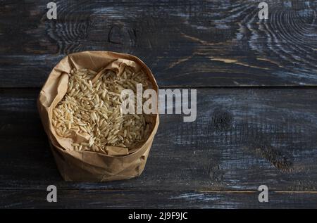 Riz brun brut à grain long dans un sac de papier sur fond en bois, espace Banque D'Images