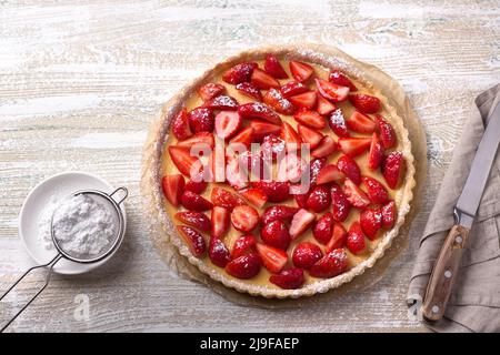 Tarte d'été avec crème de lait cuite et fraises fraîches juteuses sur fond de bois clair, vue de dessus, horizontale Banque D'Images