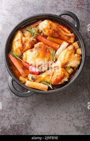 Le poulet à la rhubarbe, les oignons et l'ail sont mijotés avec du vin blanc et du beurre dans une sauce riche en gros plan dans une poêle à frire sur la table. Haut vertical Banque D'Images