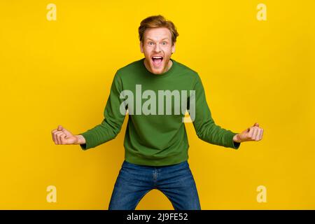 Photo d'un homme chanceux impressionné vêtu d'un chandail vert souriant levant poings isolé couleur jaune fond Banque D'Images