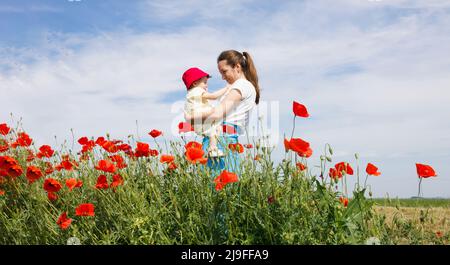 Une femme tenant son enfant dans un champ de coquelicots rouges Banque D'Images