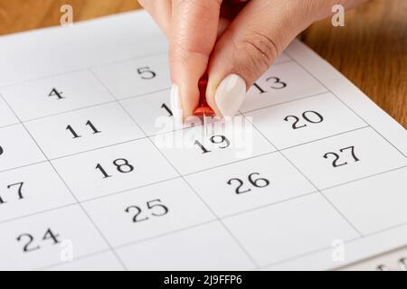 Épinglette rouge collée le jour du mois dans le calendrier, concept d'affaires. Belles mains de femmes Banque D'Images