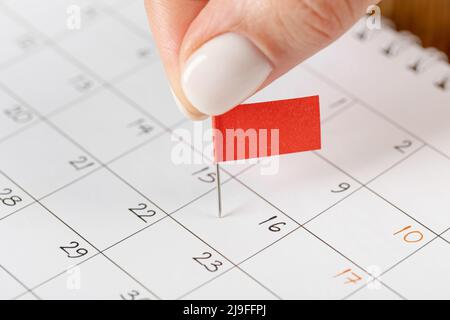 Les mains corrigeant l'horaire des notes, la vignette du drapeau rouge dans le calendrier pour la réunion et le rappel de rendez-vous Banque D'Images