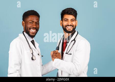 portrait d'un professionnel de santé souriant en blouse de laboratoire blanche avec stéthoscope conférant avec un jeune médecin sur fond bleu Banque D'Images