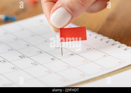 Les mains corrigeant l'horaire des notes, la vignette du drapeau rouge dans le calendrier pour la réunion et le rappel de rendez-vous Banque D'Images