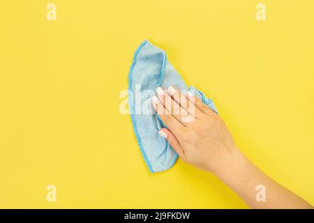 La main d'une femme au foyer tient un chiffon pour épousseter ou laver. Espace vide pour le texte ou le logo sur fond jaune. Début du printemps ou nettoyage régulier. Nettoyage Banque D'Images