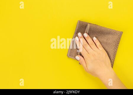 La main d'une femme au foyer tient un chiffon pour épousseter ou laver. Espace vide pour le texte ou le logo sur fond jaune. Début du printemps ou nettoyage régulier. Nettoyage Banque D'Images