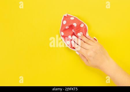 La main d'une femme au foyer tient un chiffon pour épousseter ou laver. Espace vide pour le texte ou le logo sur fond jaune. Début du printemps ou nettoyage régulier. Nettoyage Banque D'Images