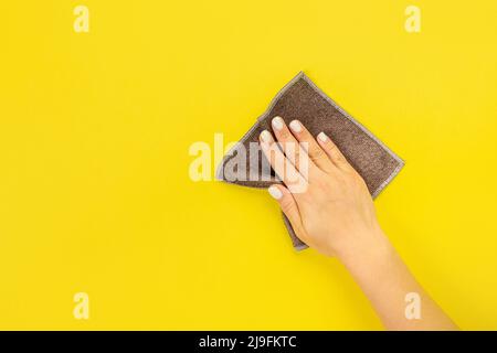 La main d'une femme au foyer tient un chiffon pour épousseter ou laver. Espace vide pour le texte ou le logo sur fond jaune. Début du printemps ou nettoyage régulier. Nettoyage Banque D'Images