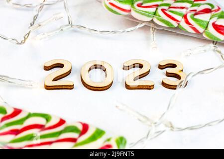 Silhouette en bois numéros 2023 avec lumières de Noël et bonbons doux sur fond clair. Félicitations et concept de planification pour le début de la nouvelle année. Banque D'Images