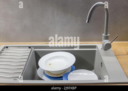 Pile de plats sales comme des assiettes dans le lavabo en granit gris moderne dans la cuisine. Banque D'Images