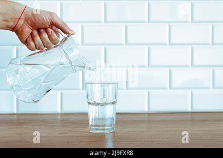 Verser de l'eau fraîche purifiée de la verseuse dans le verre de la table Banque D'Images