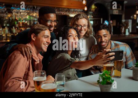 Groupe mixte de jeunes adultes assis au restaurant prenant des selfies avec appareil cellulaire Banque D'Images