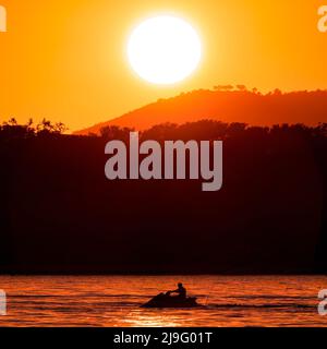 Un jet ski sur la mer avec un coucher de soleil orange en arrière-plan Banque D'Images