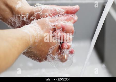 Un homme lave ses mains avec du savon sous le robinet sous l'eau courante de près. Concept de santé, de propreté et d'hygiène. Banque D'Images