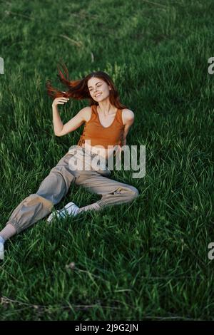 Une femme se trouve sur de l'herbe verte de printemps fraîche dans un parc sans moustiques ni tiques et aime se détendre tout en regardant le coucher du soleil. Le concept de coffre-fort Banque D'Images