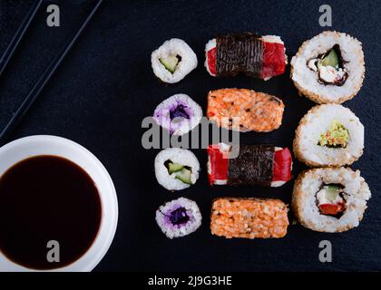 sushi avec des baguettes et du soja sur une assiette noire prête à manger sur fond noir Banque D'Images