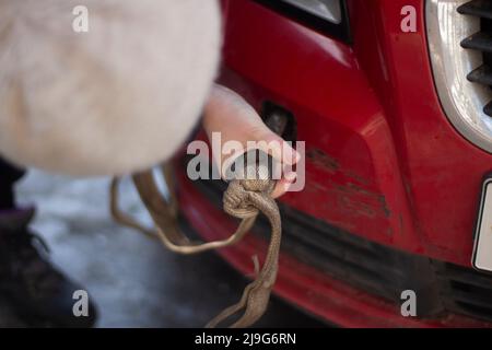 Câble pour voiture. Guy accroche la voiture pour le remorquage. Mains tient le mousqueton pour visser dans le pare-chocs de la voiture. Préparation de l'évacuation du véhicule. Banque D'Images