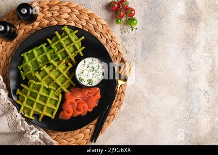 Gaufres belges vertes. Épinards ou ail sauvage ou gaufres au pesto avec saumon rouge et sauce à la crème sur fond de table en béton gris. Délicieux petit déjeuner, Banque D'Images