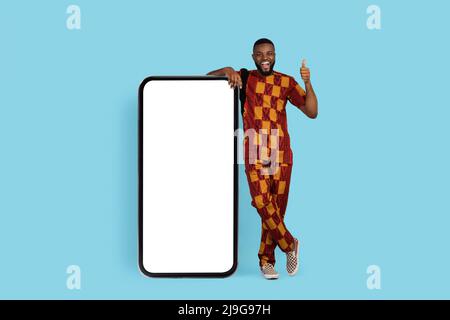 Offre incroyable. Homme noir excité en costume traditionnel debout près de smartphone vierge Banque D'Images