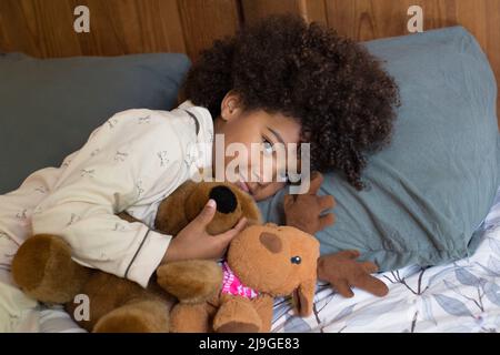 Fille souriante couchée avec un jouet sur le lit Banque D'Images