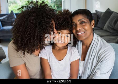 Grand-mère souriante et petite-fille regardant l'appareil photo tandis que la mère embrasse sa fille Banque D'Images